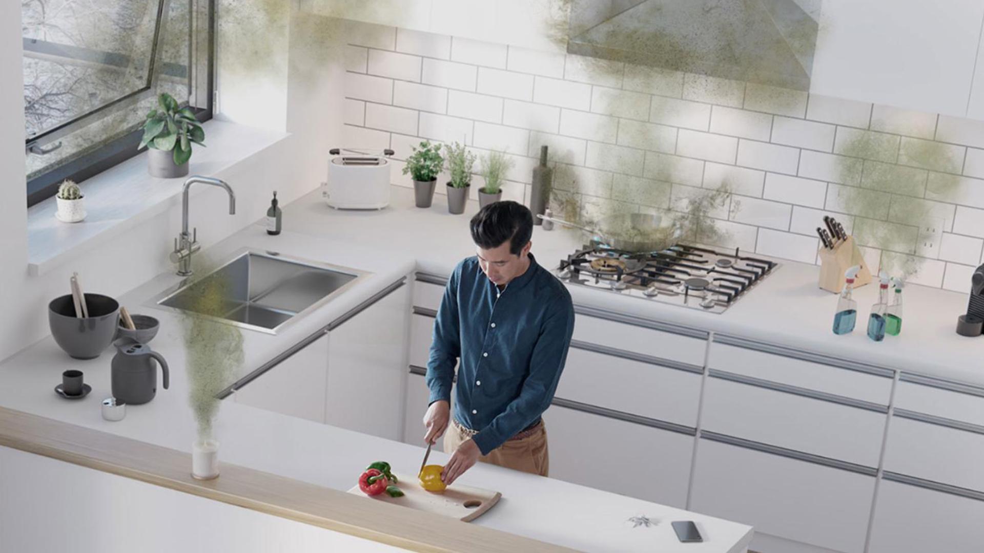 Mężczyzna w kuchni krojący paprykę wokół którego unoszą się niewidoczne cząsteczki i zanieczyszczenia z kuchenki, środków czyszczących i odświeżacza powietrza