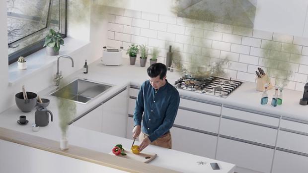 Mężczyzna w kuchni krojący paprykę wokół którego unoszą się niewidoczne cząsteczki i zanieczyszczenia z kuchenki, środków czyszczących i odświeżacza powietrza