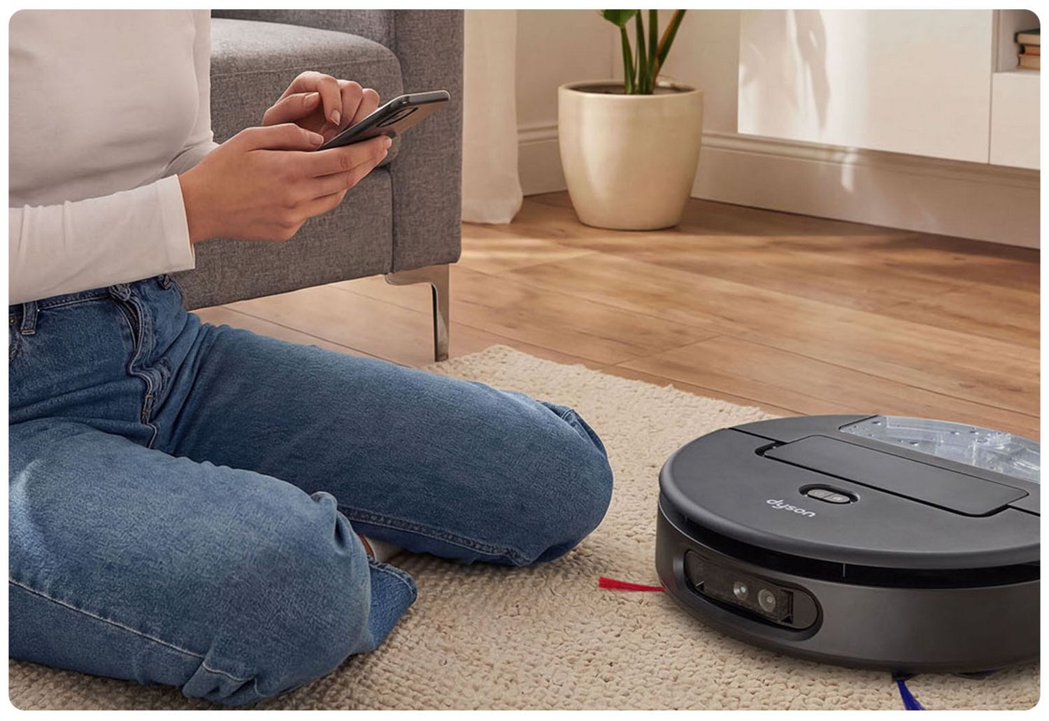 Dyson Spot Scrub AI robot on a rug with Dyson's Concierge service demonstrated via a mobile phone