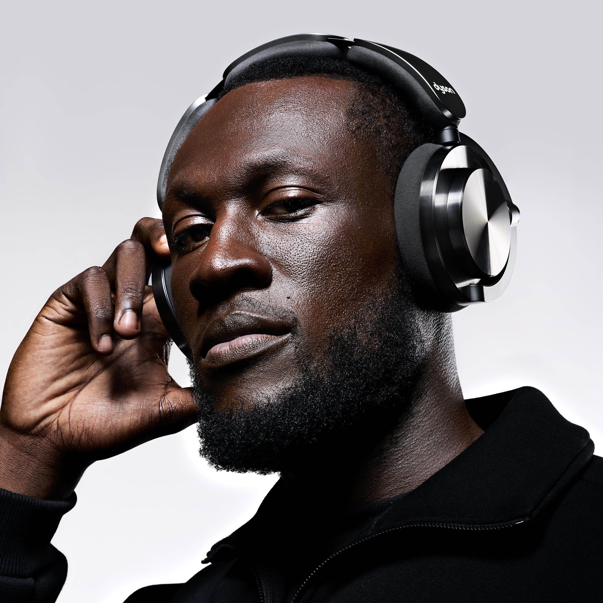 A side-profile of Stormzy wearing Dyson OnTrac headphones with CNC Black Nickel outer caps and Khaki ear cushions.
