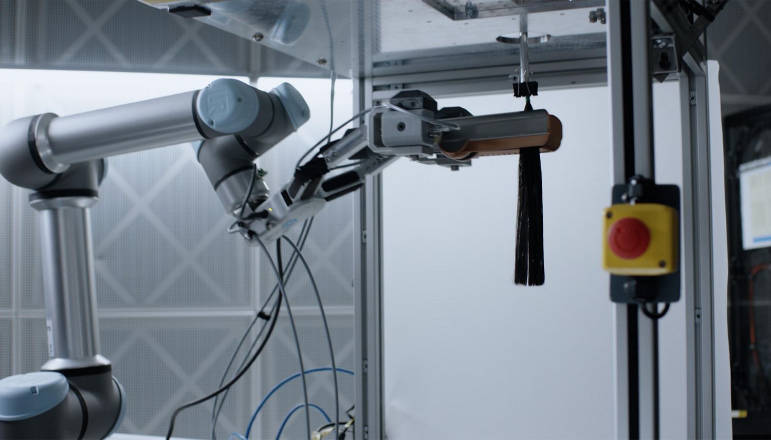 The Dyson Airstrait straightener is held by a robot arm and tested on a hair tress in a Dyson lab.