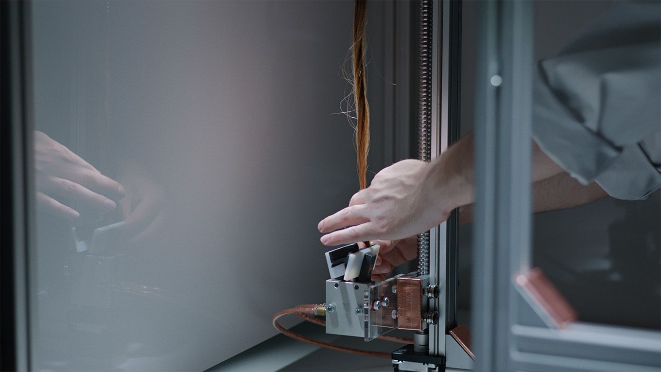 A Dyson engineer uses a machine to test a tress of natural hair.