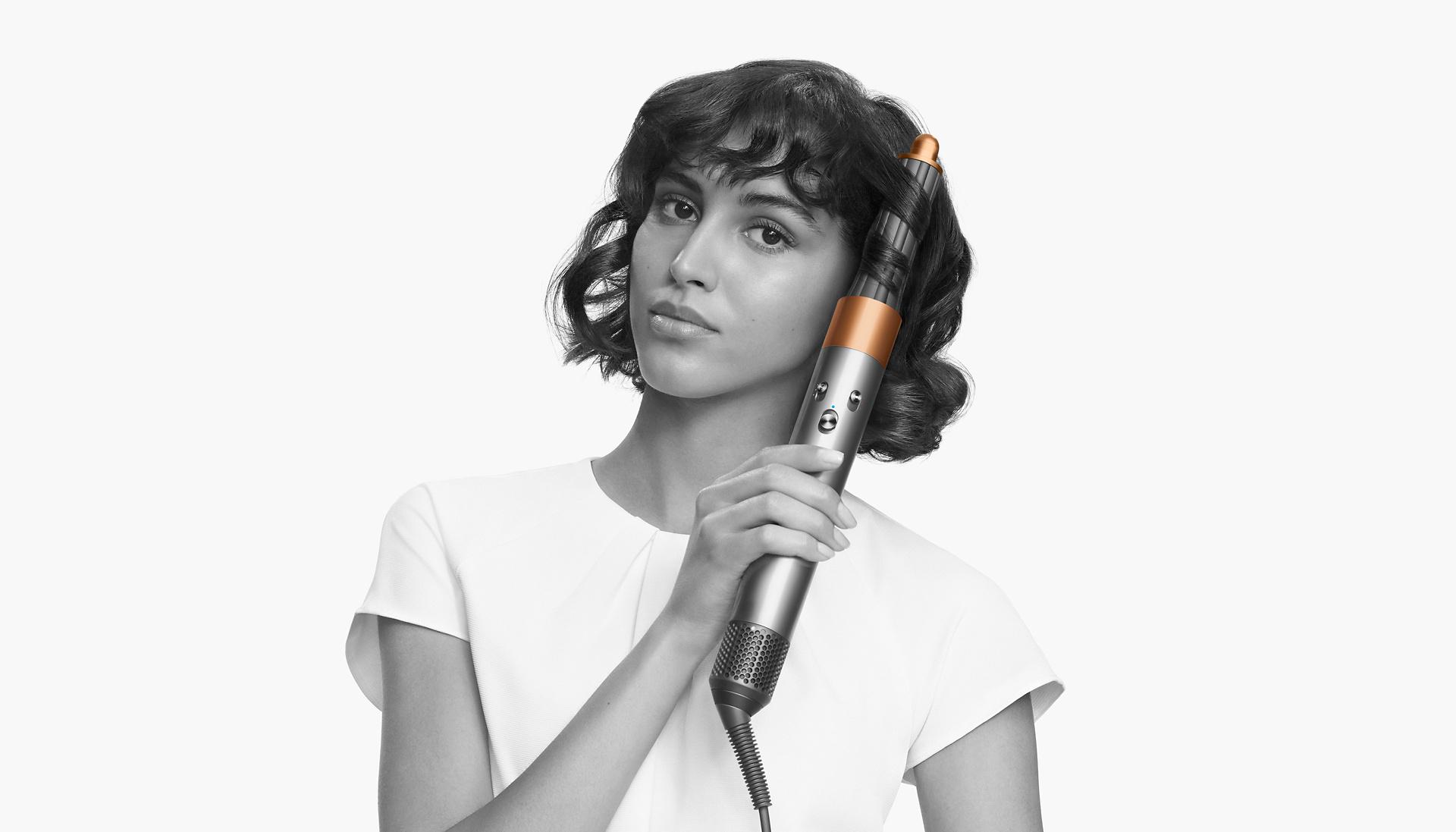 A model looking at the camera while using the Dyson Airwrap multi-styler and dryer on her short hair.