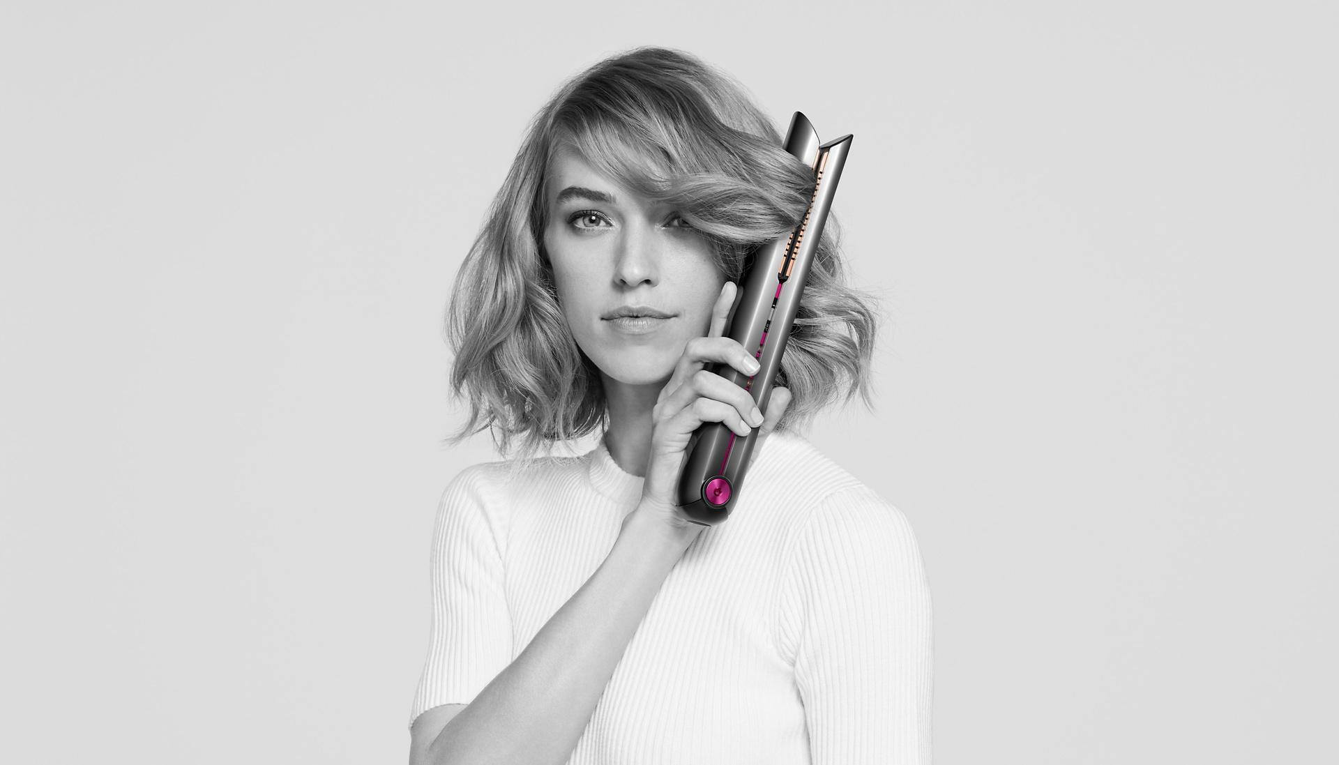 A model looking at camera while using the Dyson Corrale hair straightener on her short hair.