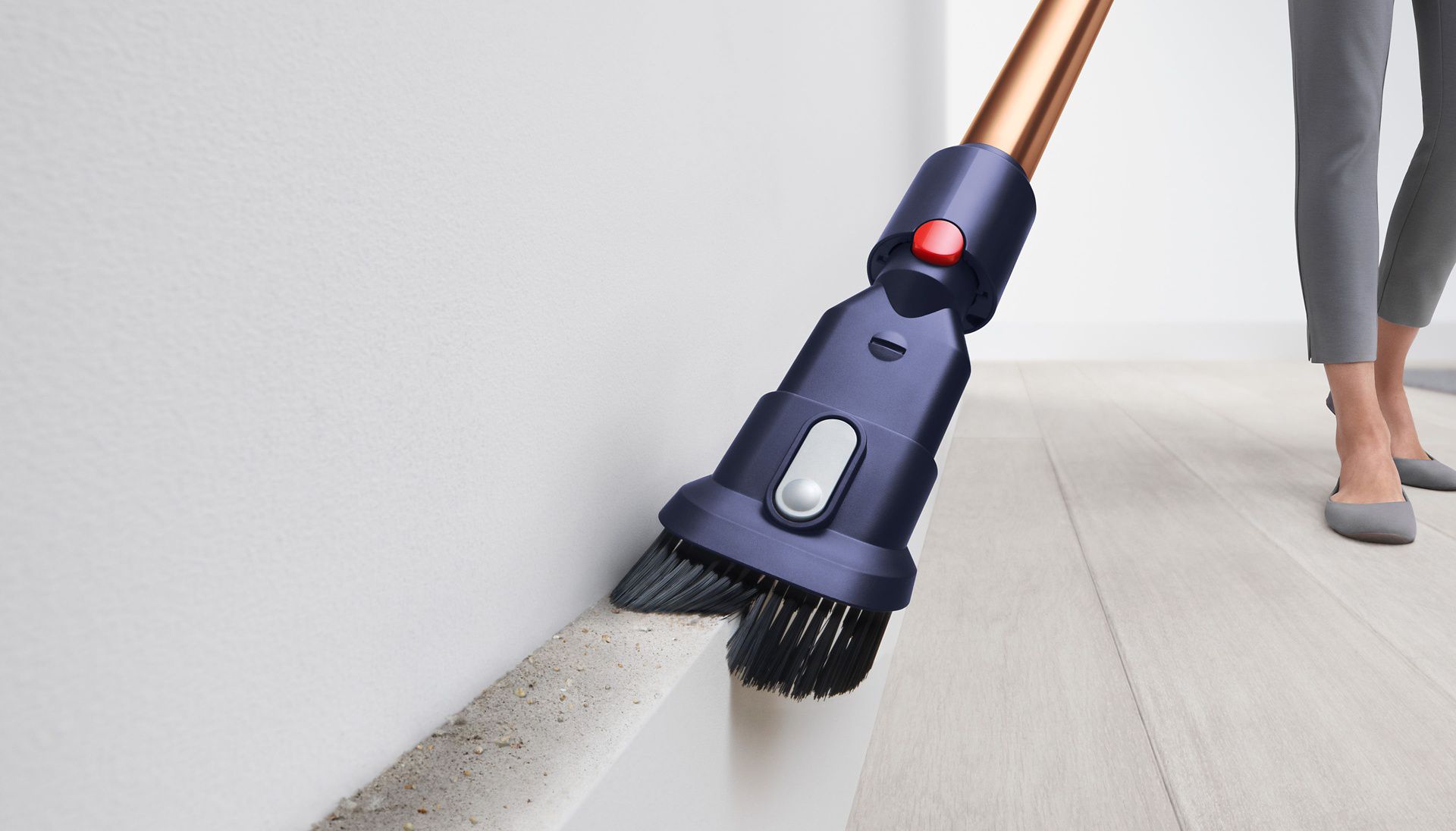 A Dyson vacuum cleaner with the Combination Tool is used to clear dust and debris from a skirting board.