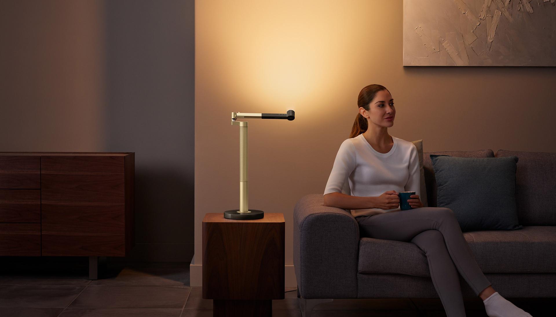 Kobieta siedząca na kanapie przy oświetleniu Dyson z kubkiem w ręku