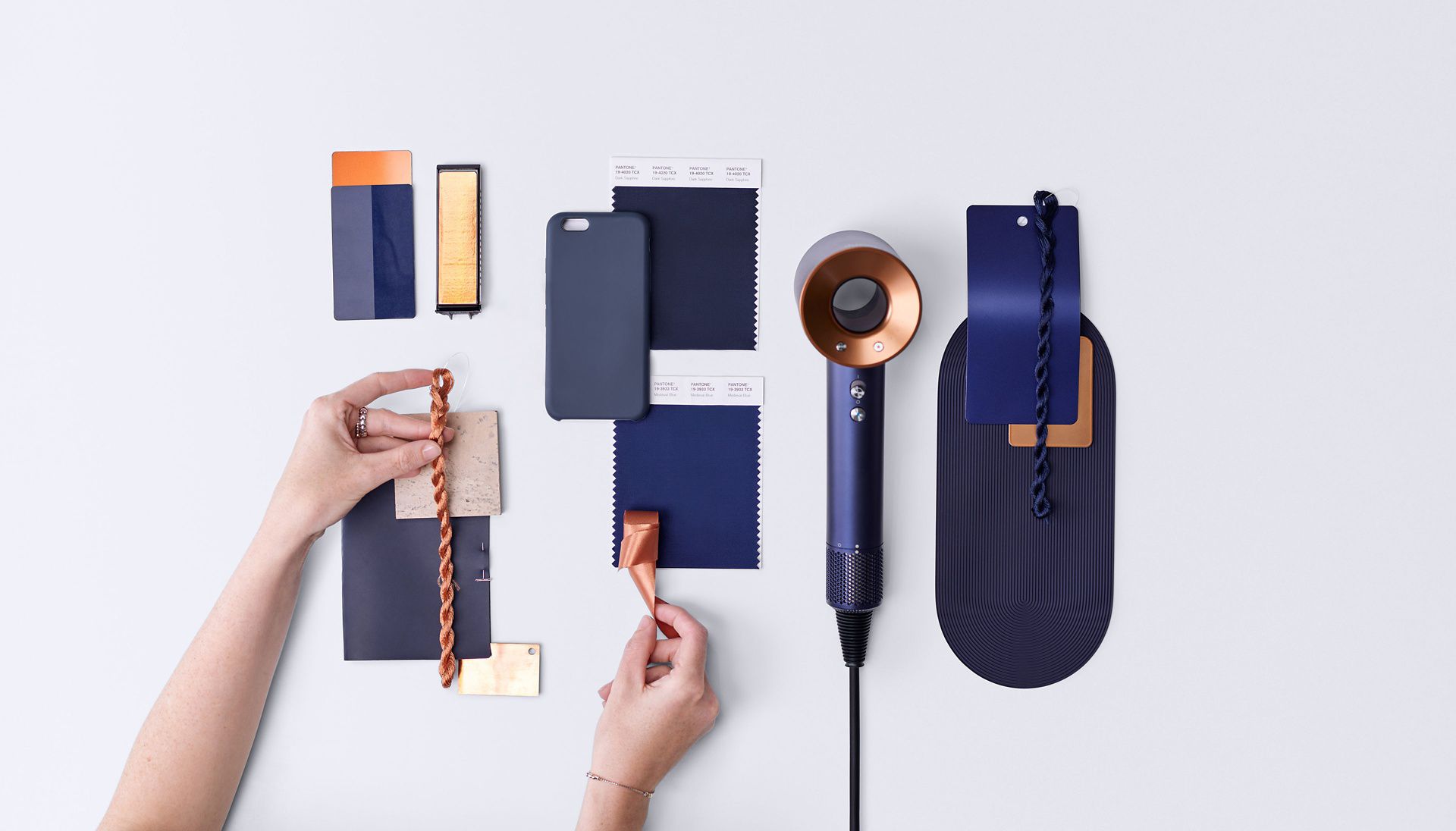 O secador de cabelo Dyson Supersonic e as suas cores, materiais e acabamentos na mão de um engenheiro sobre um fundo branco.