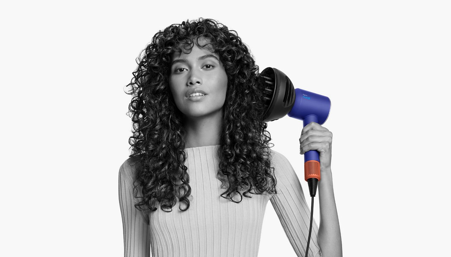 Dyson Supersonic Nural hair dryer with Wave+Curl diffuser used by woman to dry her curly coily hair