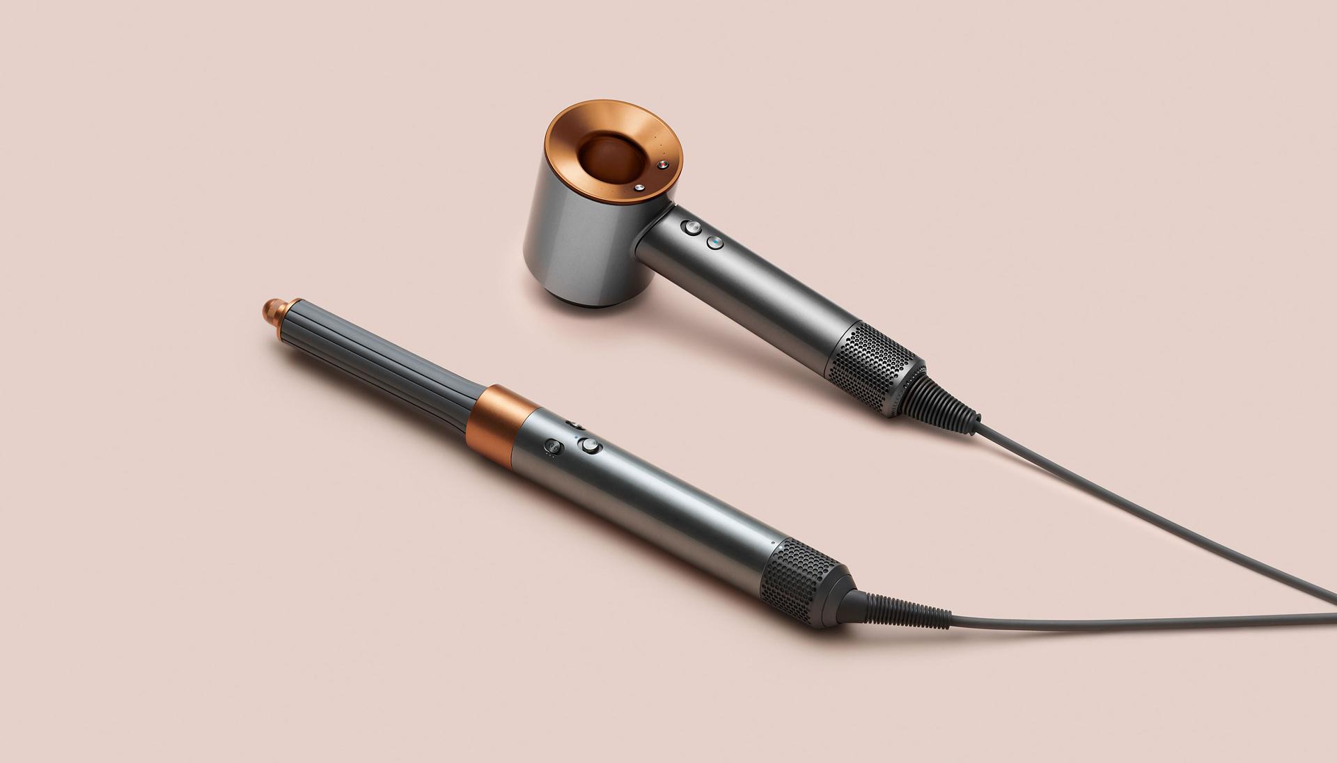 Dyson Airwrap multi-styler and dryer next to Dyson Supersonic hair dryer on pink background