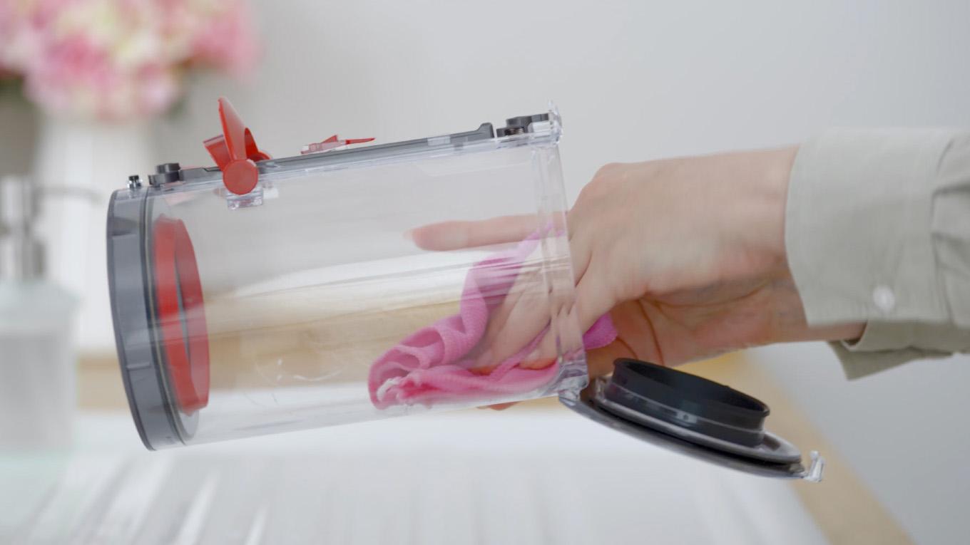 A Dyson owner cleans the inside of their vacuum’s bin using a damp lint-free cloth after removing the bin from the machine.