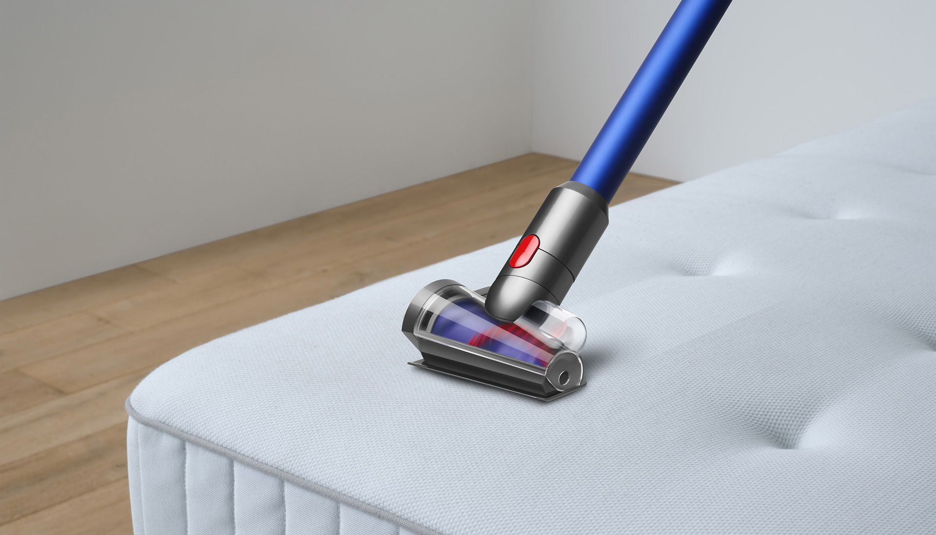 The Dyson Hair screw tool being used to clean someone's mattress in a plain bedroom.