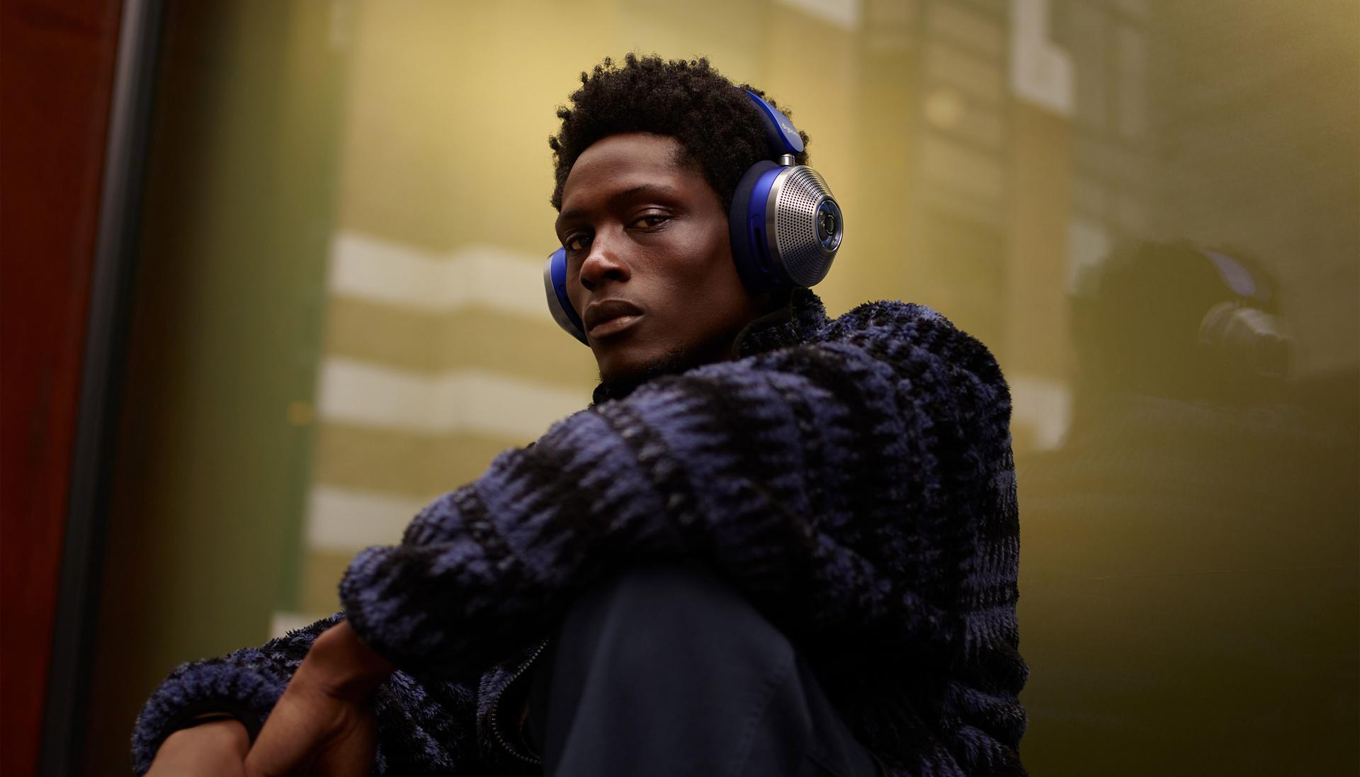 Mężczyzna siedzący przy oknie w mieście i noszący słuchawki z aktywną redukcją hałasu Dyson Zone.