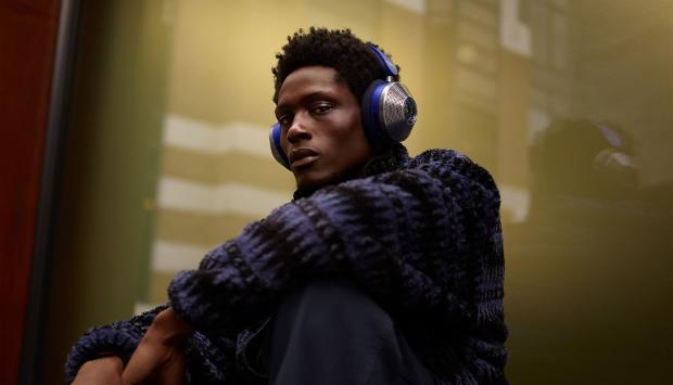 Mężczyzna siedzący przy oknie w mieście i noszący słuchawki z aktywną redukcją hałasu Dyson Zone.