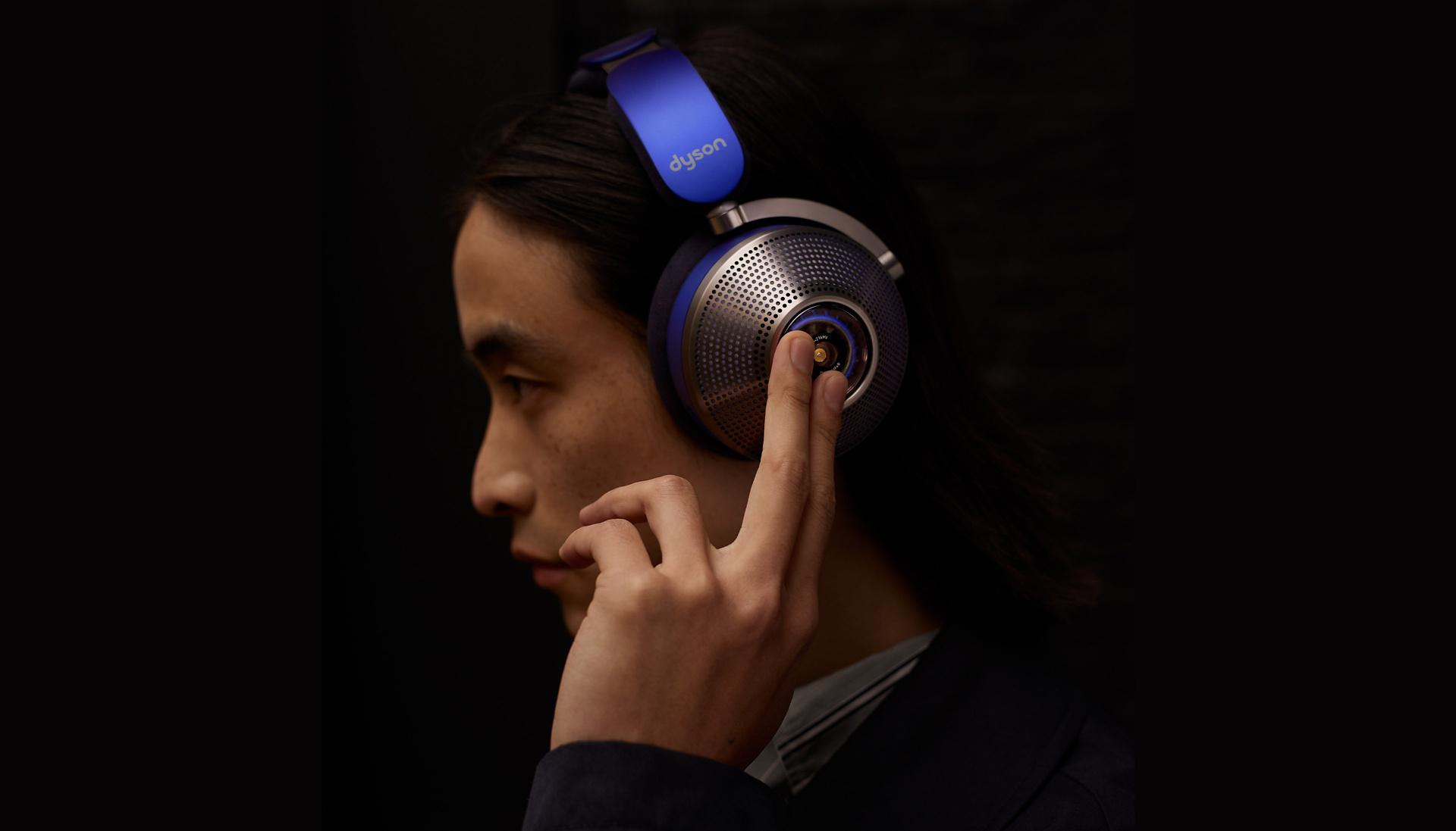 A model tapping the cup on their Dyson Zone noise cancelling headphones while in complete darkness.