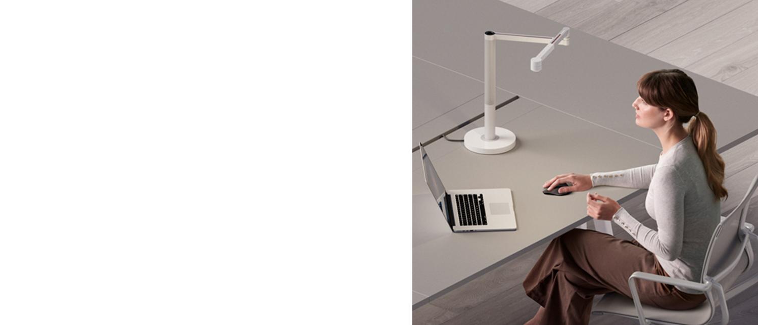 A woman works at her desk with a Dyson Solarcycle light to illuminate her workspace