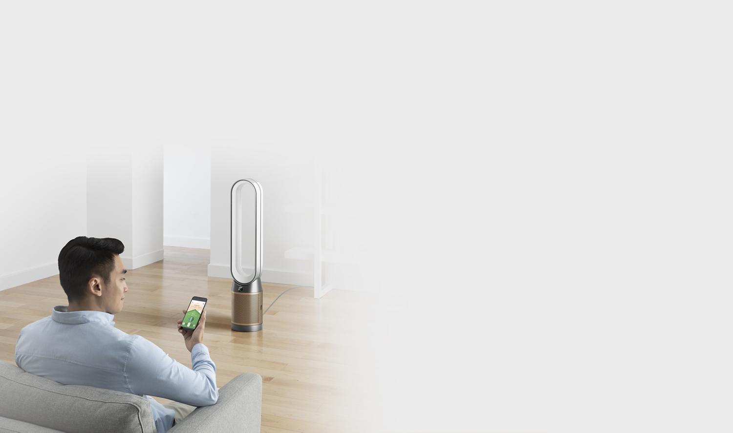 Man sits in front of Dyson purifier using the Dyson Link app on a smart phone