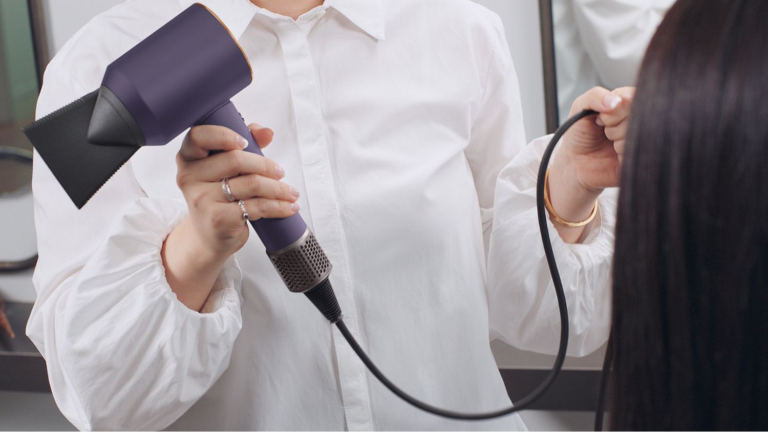 A stylist showing the Dyson Supersonic Professional hair dryer's longer cable.
