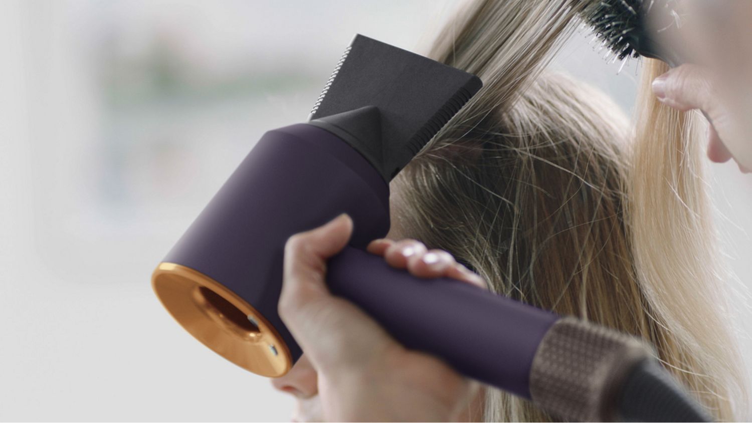 A stylist using the Dyson Supersonic r Professional hair dryer in Bright copper with the Professional concentrator.