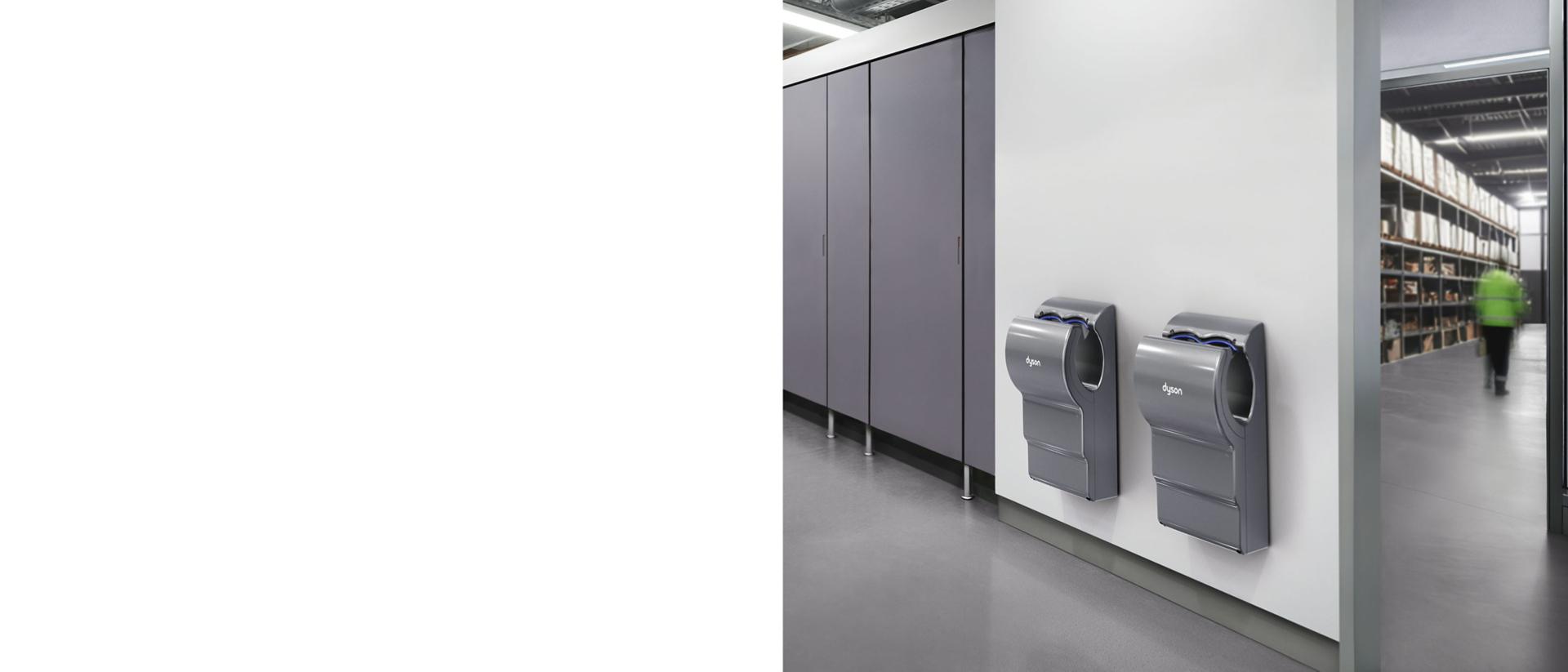 A Dyson Airblade dB hand dryer next to some cubicles in a bathroom.