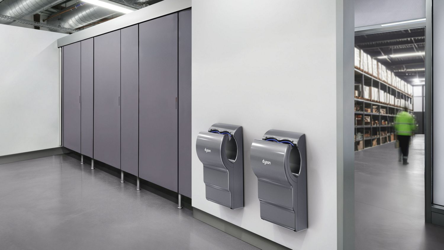 A Dyson Airblade dB hand dryer next to some cubicles in a bathroom.