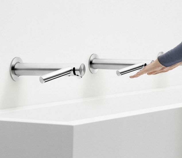 Hände, die unter dem Dyson Airblade Wash + Dry an einer Wand getrocknet werden.