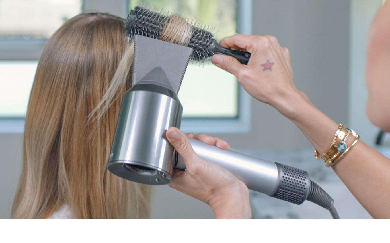 Coiffeur utilisant le sèche-cheveux Dyson Supersonic pour coiffer une cliente