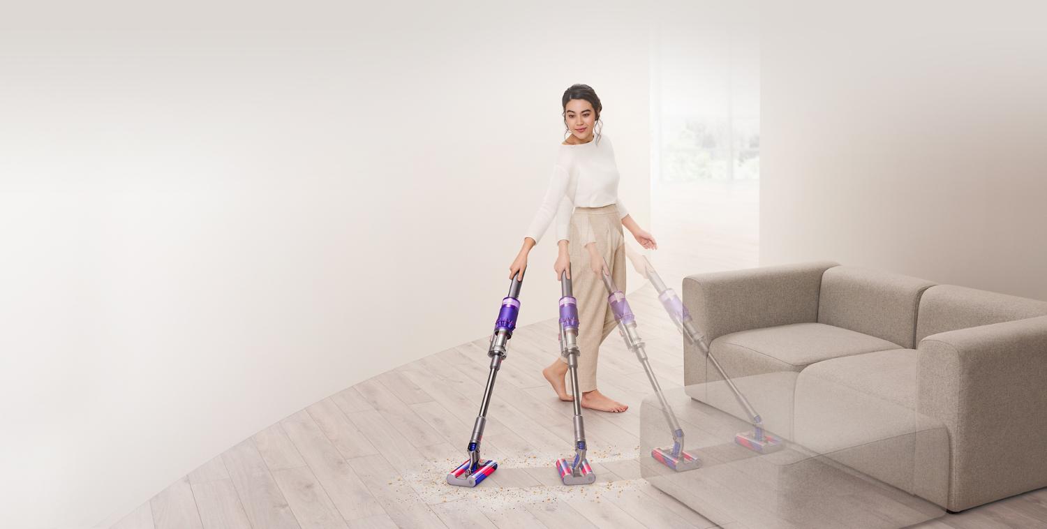 Mujer aspirando un suelo duro alrededor de un sofá con la aspiradora Dyson Omni-glide™.