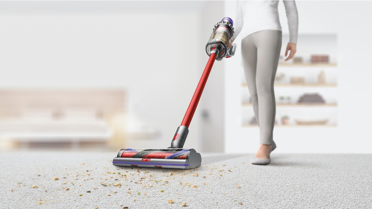 Une femme utilisant l’aspirateur Dyson V11 Outsize pour nettoyer les débris sur un tapis