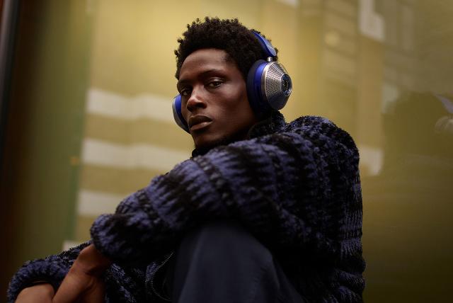 A model sitting against a window in the city while wearing his Dyson Zone noise cancelling headphones.
