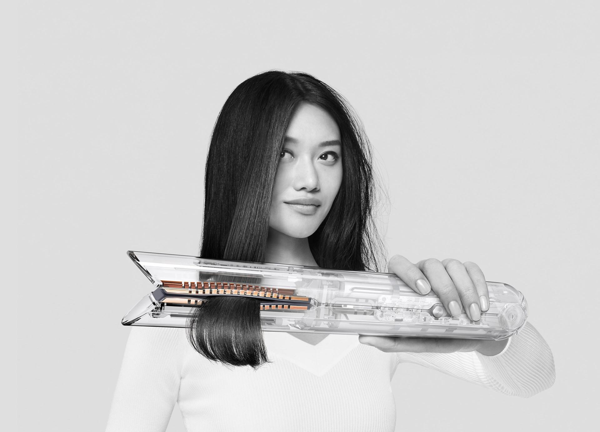 Kobieta trzymająca w ręku i prostująca włosy prostownico-lokówką Dyson Corrale