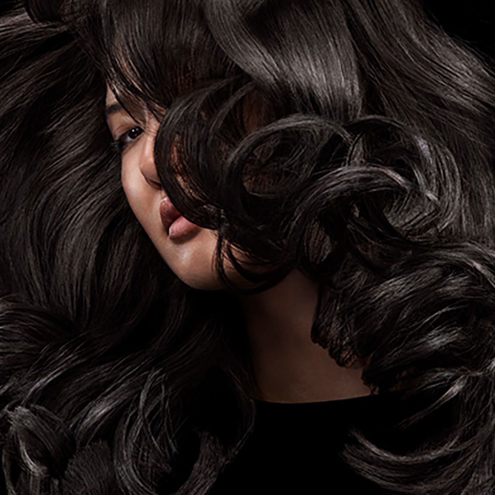 A brunette model with shiny hair styled with Dyson Chitosan products.