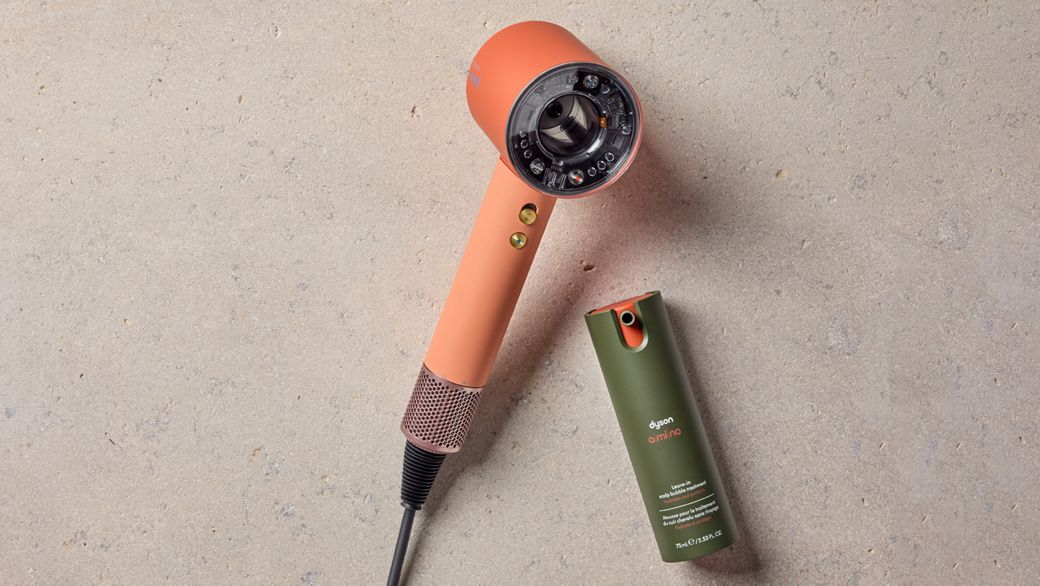 Dyson Supersonic Nural hair dryer on a rattan chair with Dyson Chitosan Pre-style cream.