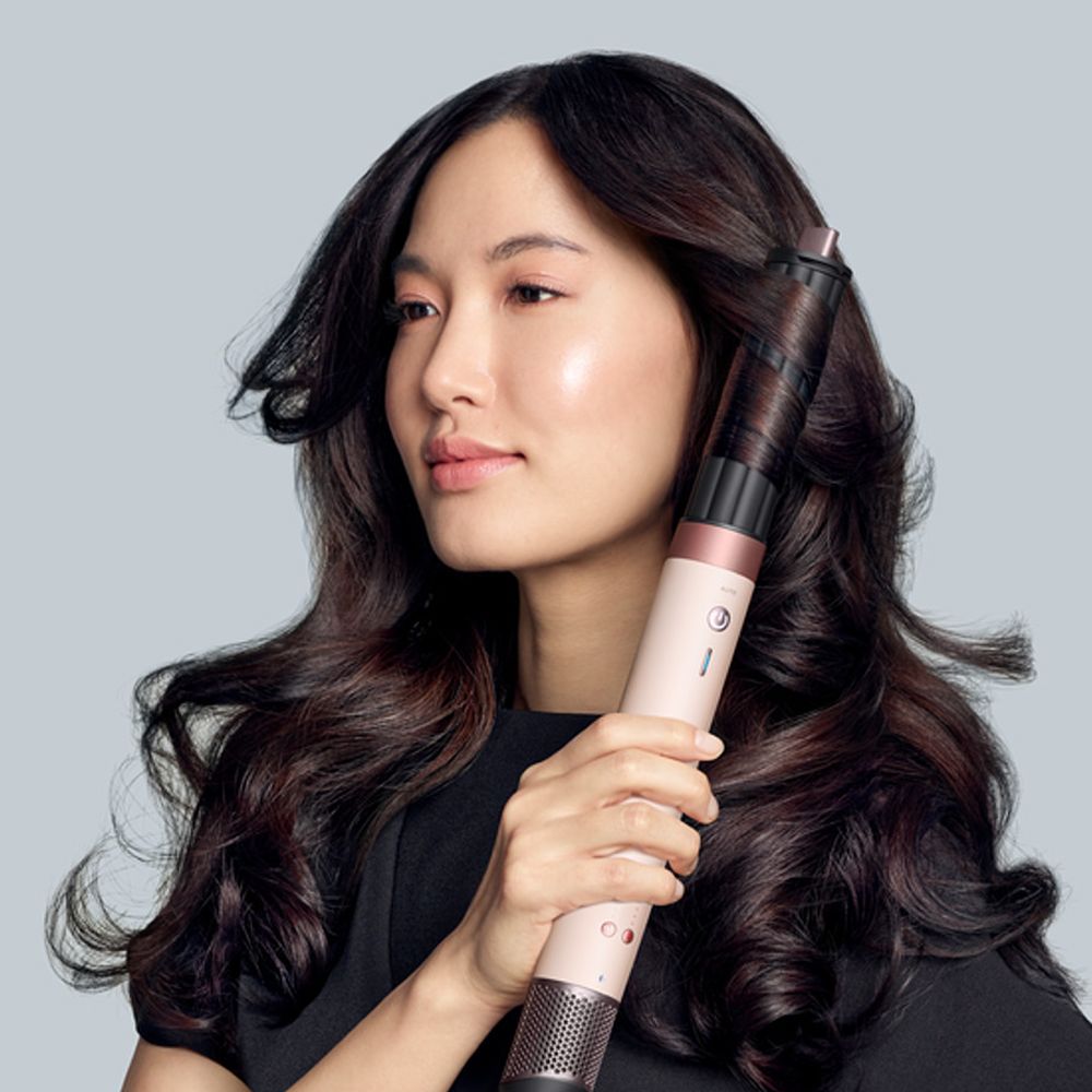 A coily haired model styles her hair with the Dyson Airwrap Co-anda2x multi-styler.