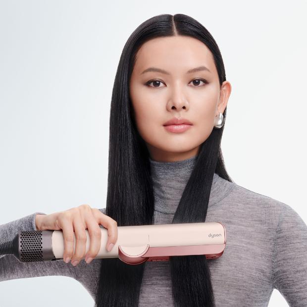 Model smooths and straightens her hair with the Dyson Airstrait dryer and straightener.