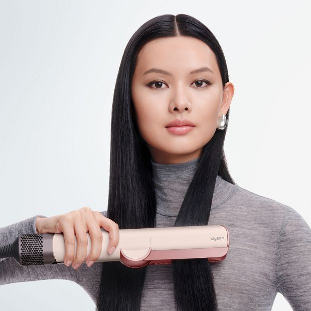 Model smooths and straightens her hair with the Dyson Airstrait dryer and straightener.