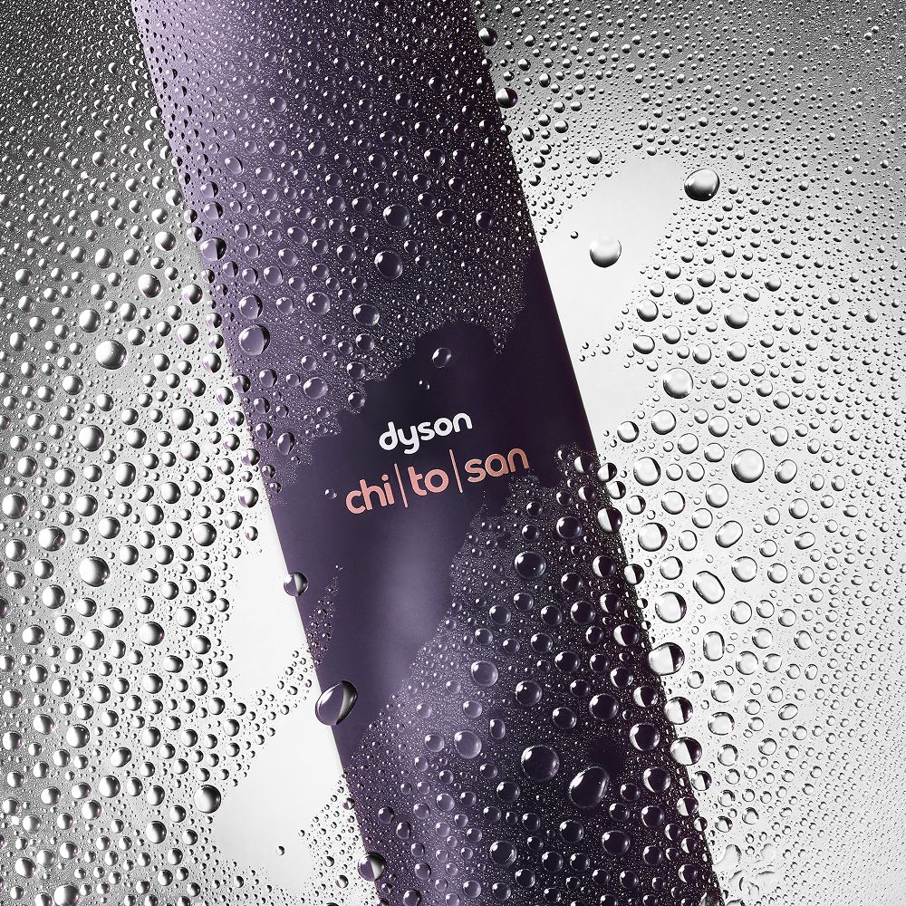 Dyson Chitosan Multi-use styling spray behind water droplets on a glass pane.
