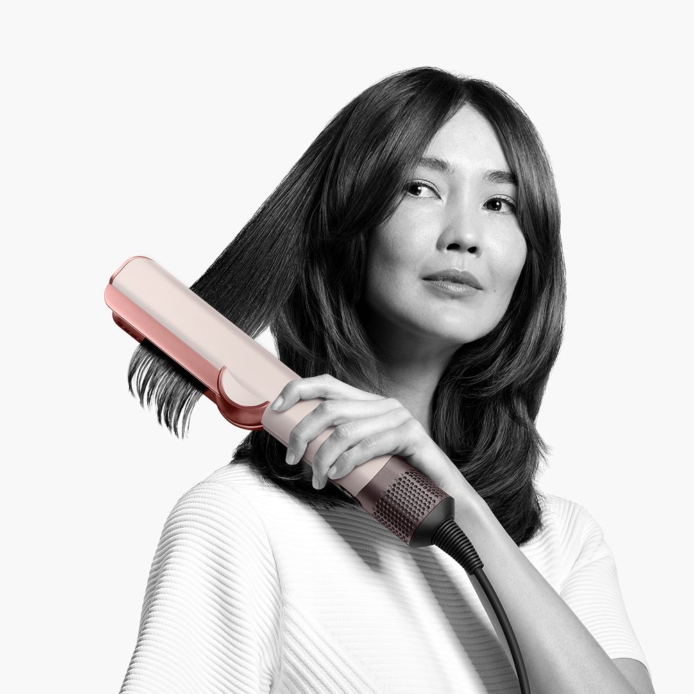 A model styles hair with the Dyson Airstrait.