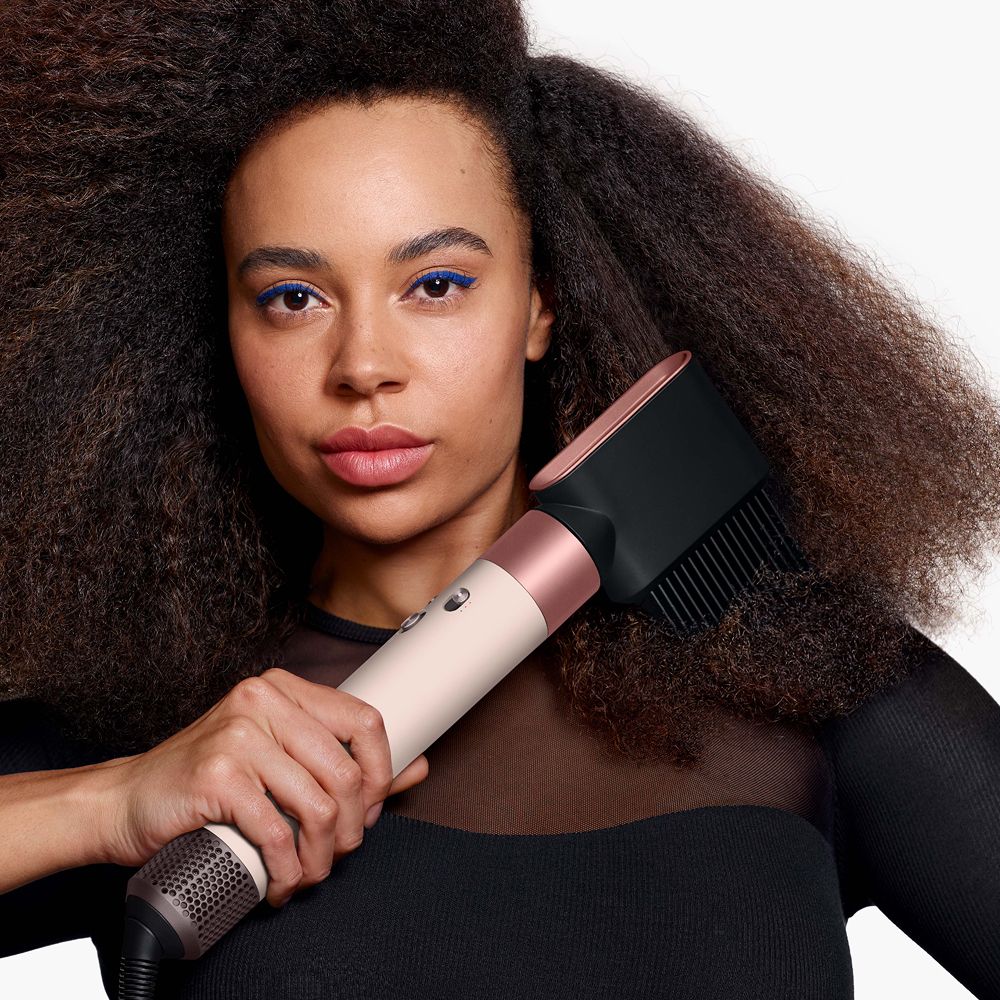 A coily haired model styles her hair with the Dyson Airwrap Co-anda2x multi-styler.