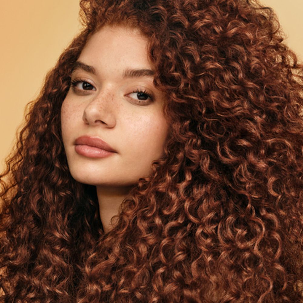 A curly haired model shows off her nourished hair after using Dyson Omega products.