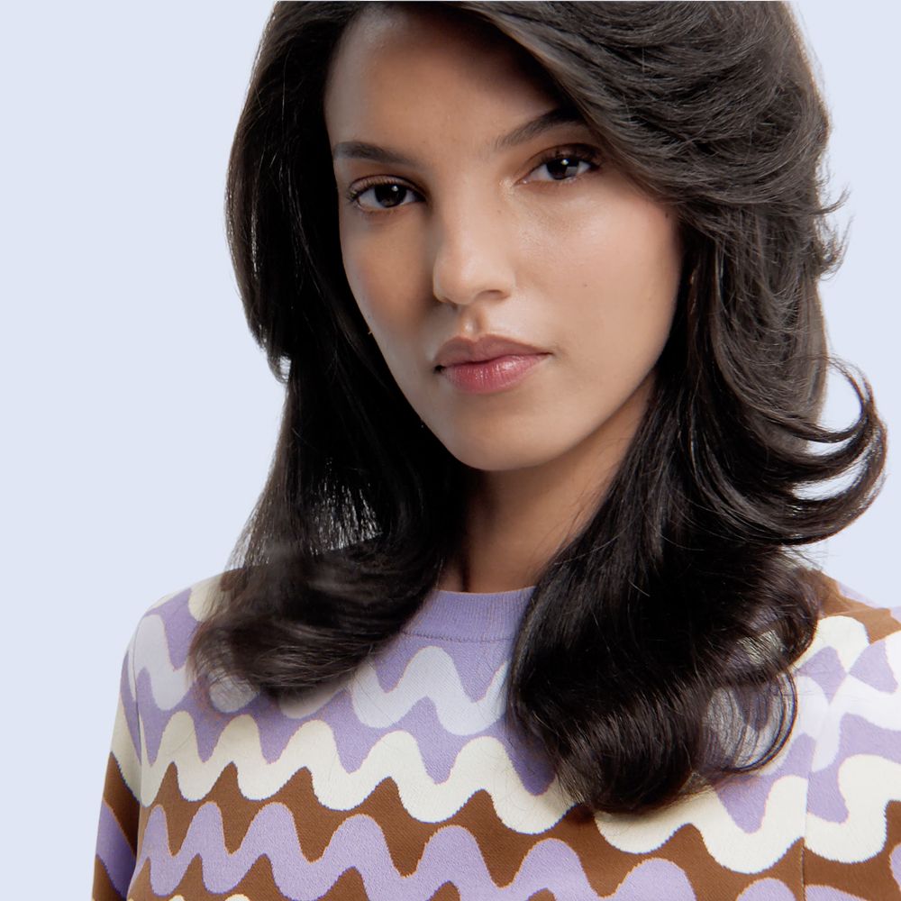 Model stands on a large flat landscape holding the Dyson Supersonic Travel hair dryer.