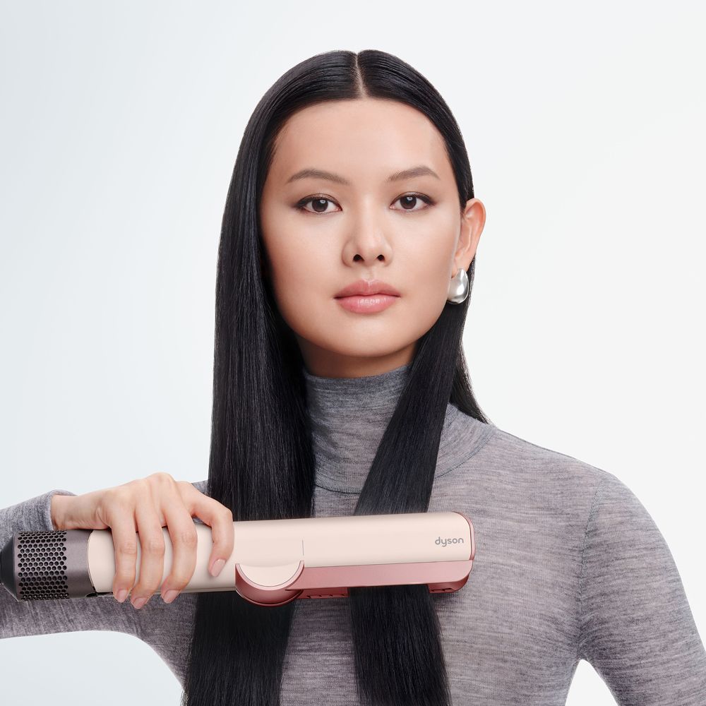 Ein Modell glättet ihr Haar mit dem Dyson Airstrait Haartrockner und -glätter.
