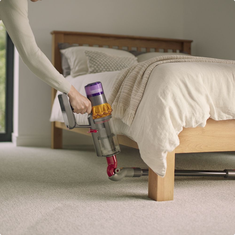 A Dyson vacuum is used with the Low-reach adaptor to clean deep under a bedframe.