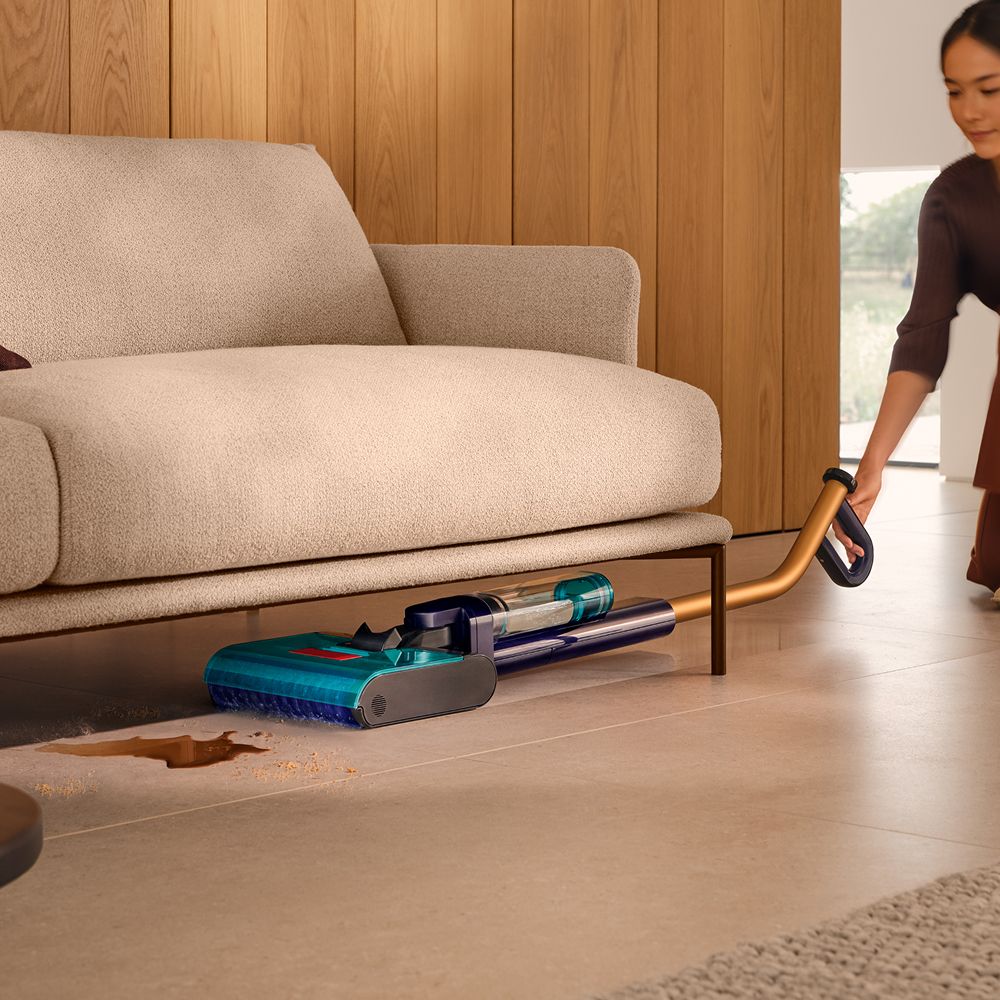 The Dyson Clean+Wash Hygiene hard floor cleaner washing under a sofa.