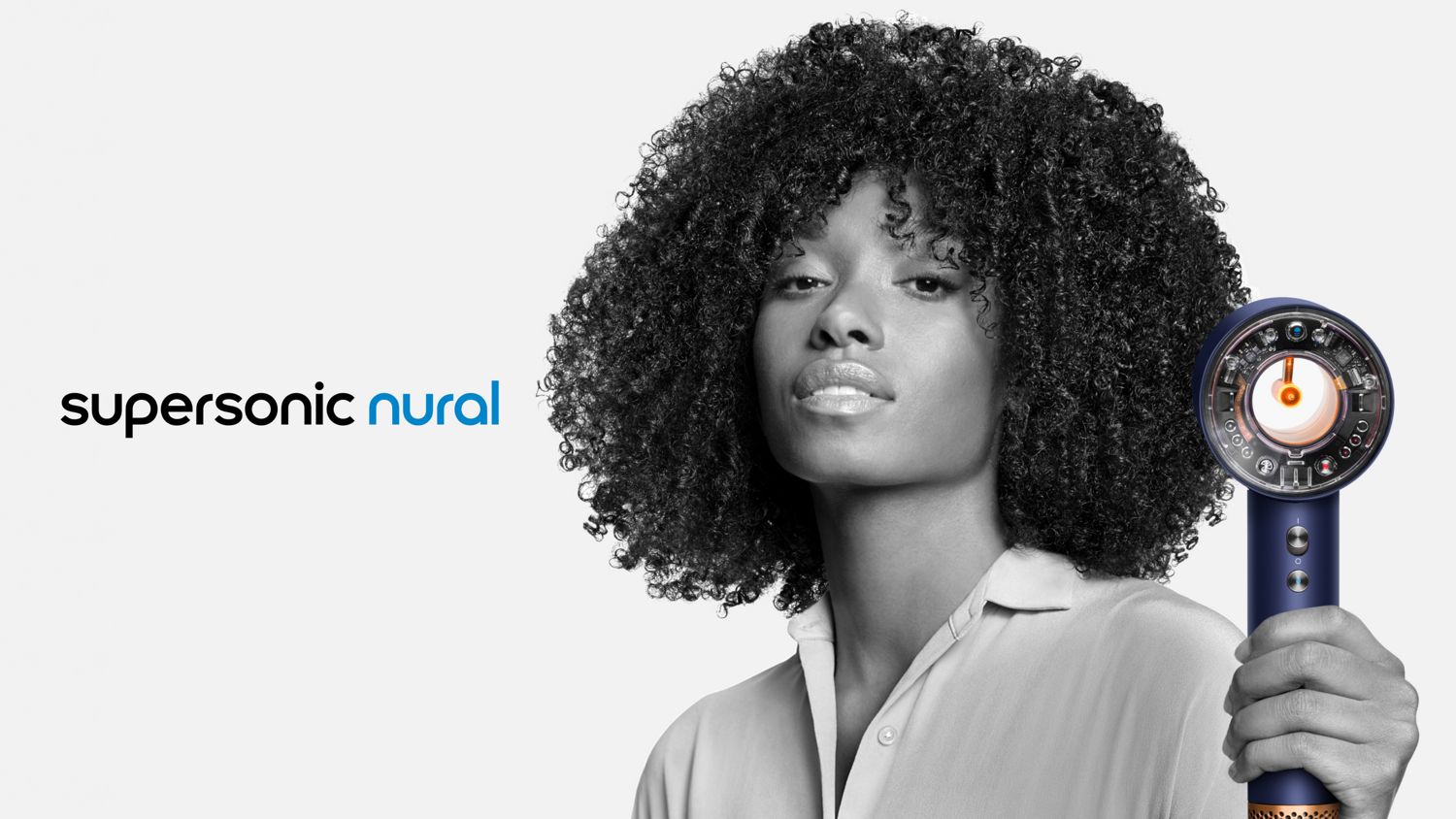 The Dyson Supersonic Nural hair dryer held by a model with coily hair.