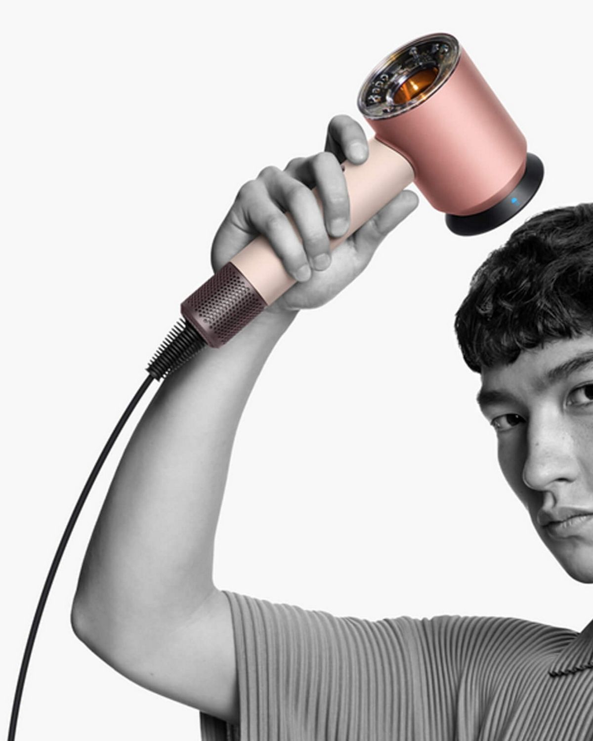 Modelo masculino sosteniendo el secador de pelo Supersonic Nural con el accesorio de aire suave cerca de su cabeza mientras se seca el cabello.