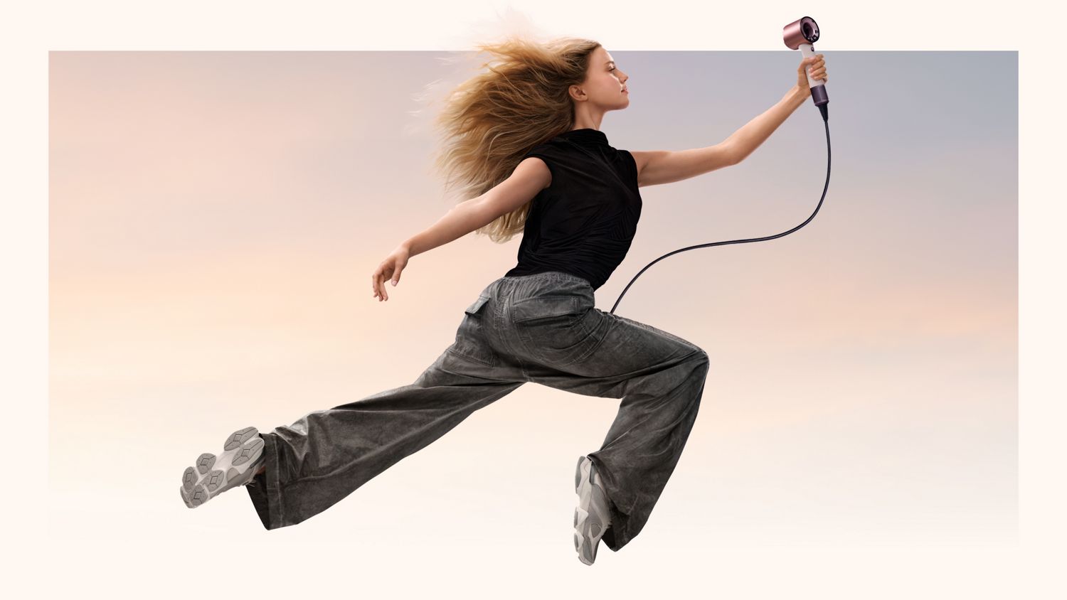 A jumping model in mid-air holding the Dyson Supersonic Travel hair dryer.
