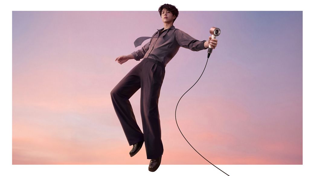 A jumping model in mid-air holding the Dyson Supersonic Travel hair dryer.