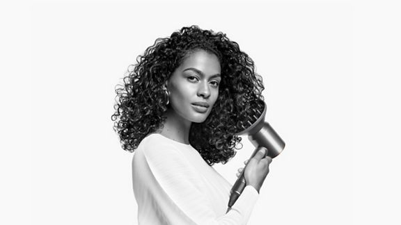 Ein Model stylt ihr krauses Haar mit dem Dyson Supersonic Haartrockner und dem Diffusor.