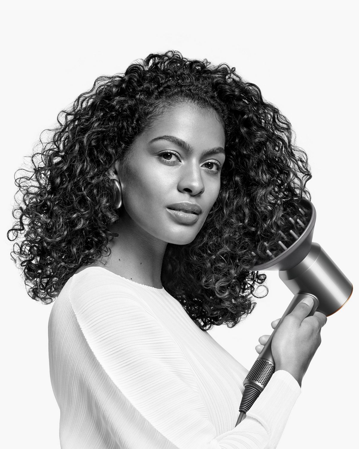A model styles her coily hair with the Diffuser attachment on the Dyson Supersonic hair dryer.