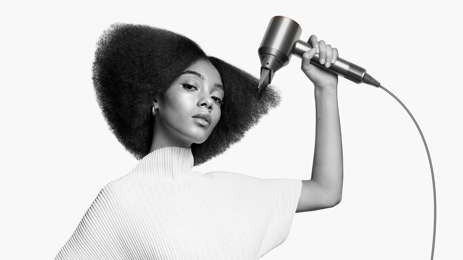 A model styles her coily hair with the Wide-tooth comb attachment on the Dyson Supersonic hair dryer.